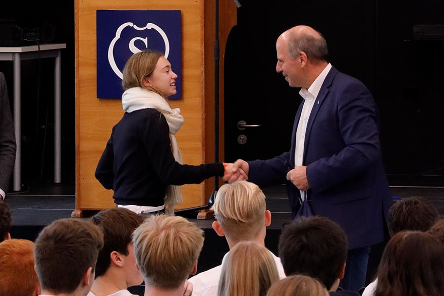 Landtagsabgeordneter in der Schulversammlung schüttelt die Hand einer Schülerin