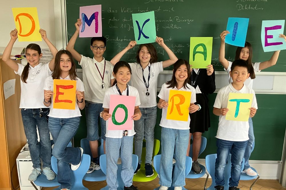 Kinder halten die Buchstaben D-E-M-O-K-R-A-T-I-E hoch