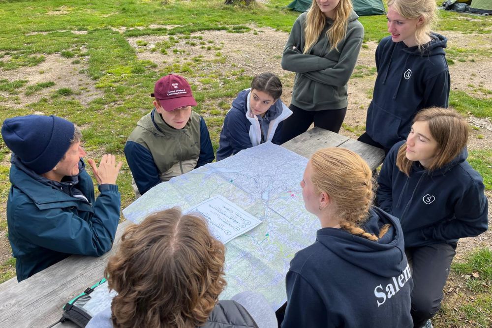 Die Gold-Expertin sitzt mit der Duke of Edinburgh's International Award Gold Gruppe um einen Tisch und bespricht die Route auf einer Landkarte.