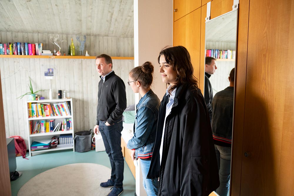 Mädchen zeigt interessiertem Vater und Kind ein Zimmer auf dem Campus Härlen