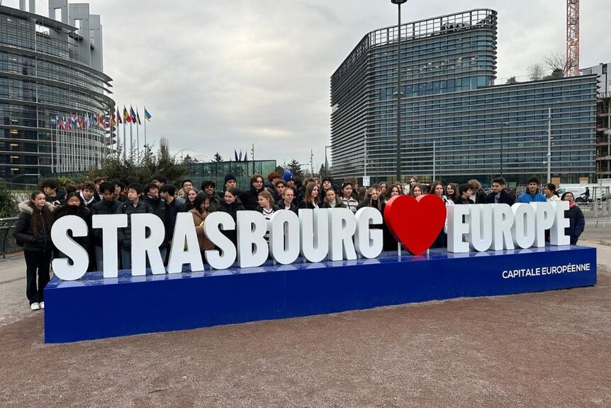 Gruppenfoto bei der Exkursion zum Europäischen Parlament in Straßburg. Die Klasse steht vor einem Schild: Strasbourg Herz Europe.