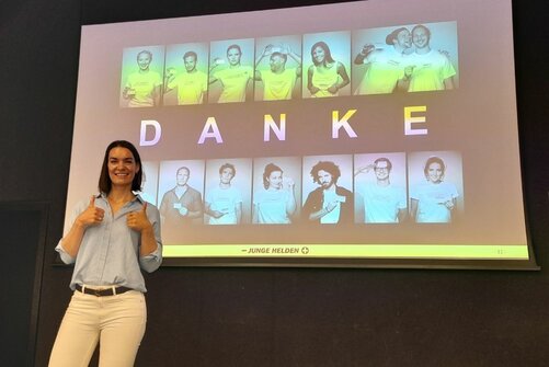 Marie-Luise Beirer steht vor der Danke-Folie ihrer Präsentation und zeigt zwei Damen hoch