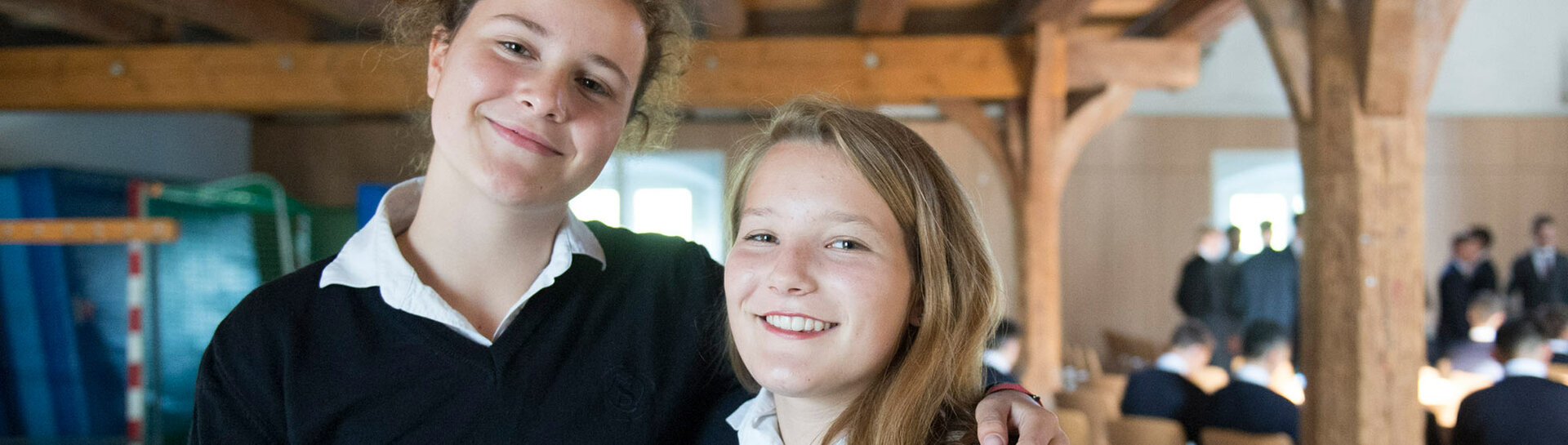 Header: zwei Schülerinnen Arm in Arm