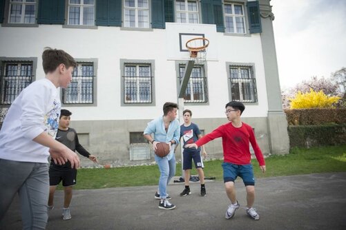 Schüler unterschiedlicher Jahrgangsstufen spielen gemeinsam Basketball vor dem Rentamt.