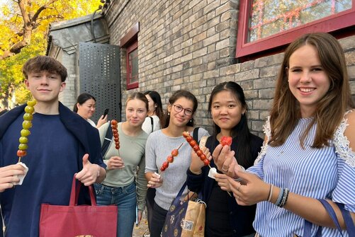 Schülerinnen und Schüler halten beim Schüleraustausch in Peking landestypische Snacks in die Kamera.