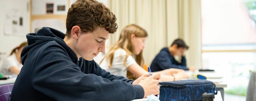 Junge sitz am Tisch und schreibt etwas im Unterricht 